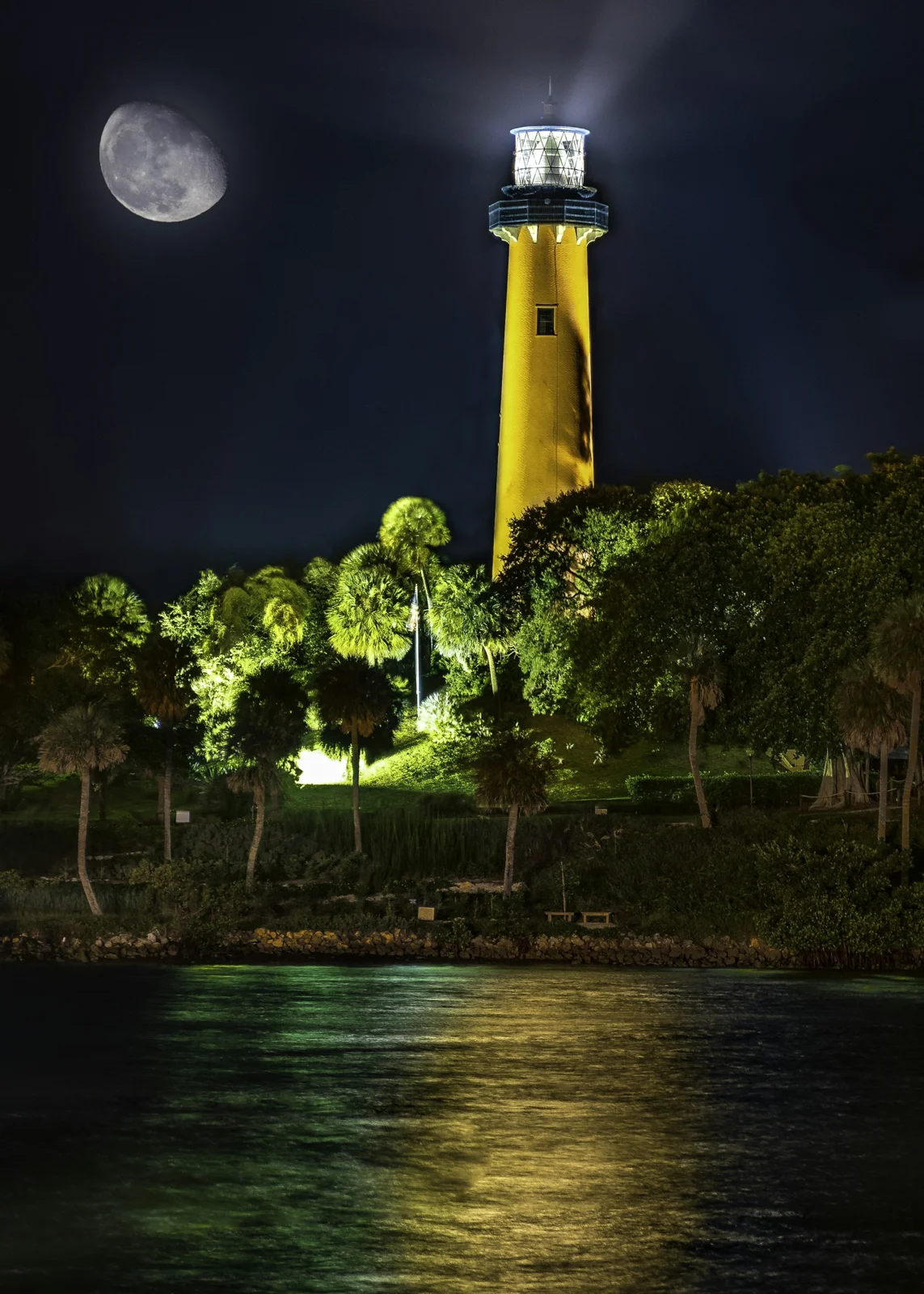 Jupiter Inlet Lighthouse illuminated at night, with moonlight over the water