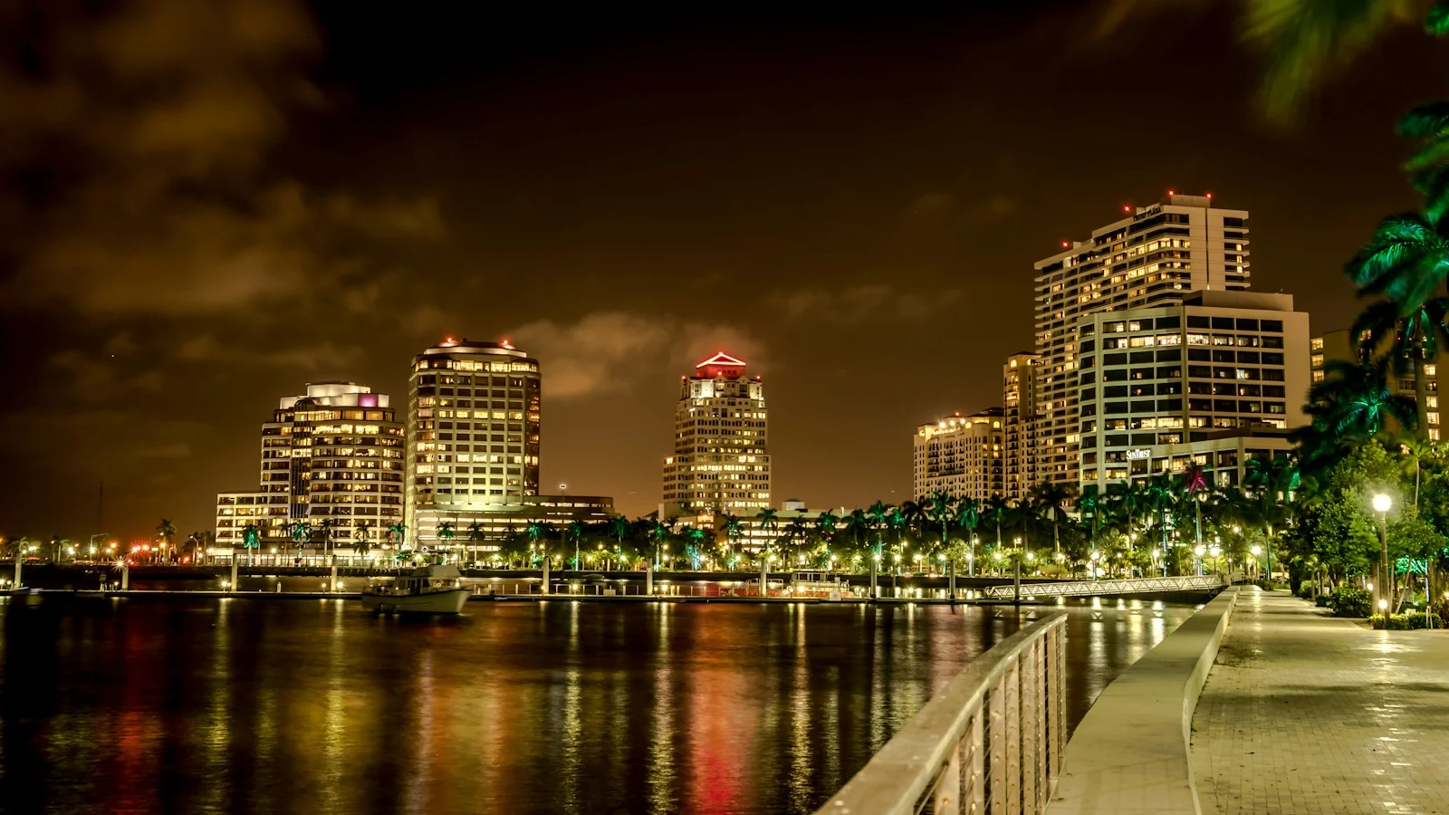 Illuminated buildings reflected in the water beside a West Palm Beach waterfront walkway